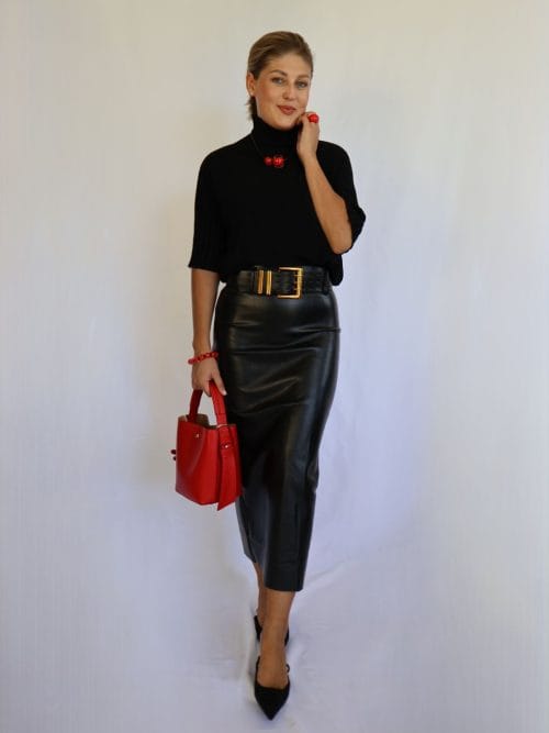 Jersey de punto negro de mujer con manga corta hasta el codo y cuello chimenea de canalé, combinado con falda de polipiel negra y cinturón dorado.