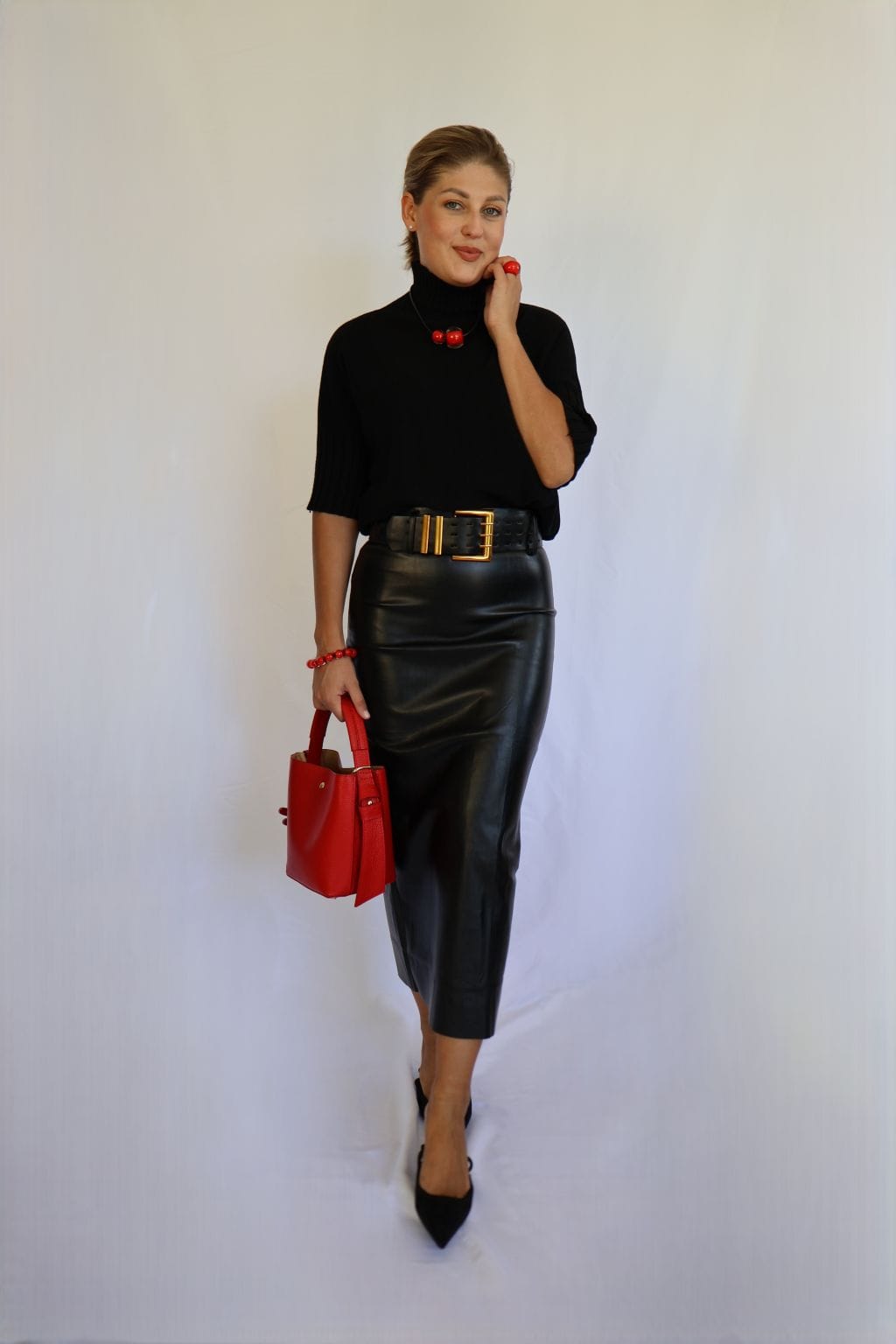 Jersey de punto negro de mujer con manga corta hasta el codo y cuello chimenea de canalé, combinado con falda de polipiel negra y cinturón dorado.