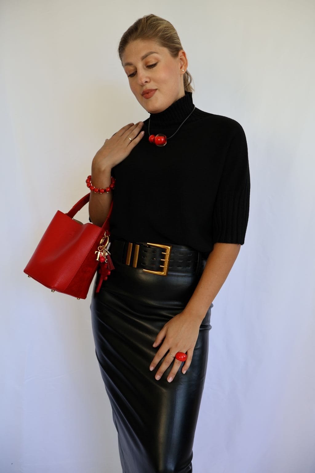 Jersey de punto negro de mujer con manga corta hasta el codo y cuello chimenea de canalé, combinado con falda de polipiel negra y cinturón dorado.