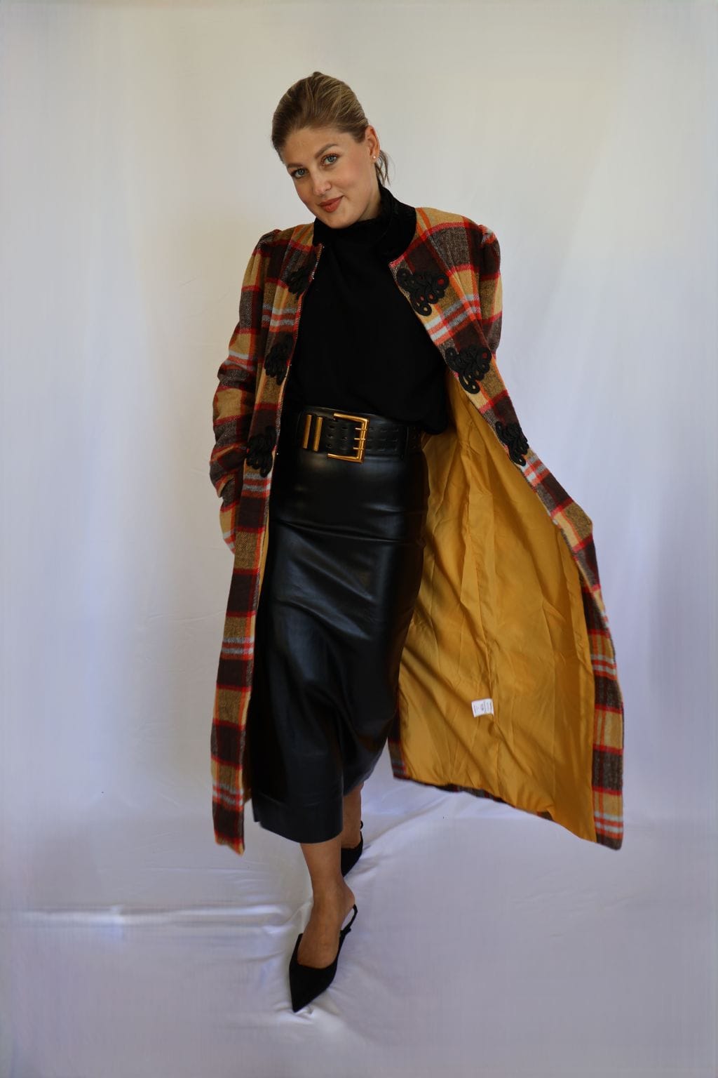 Jersey de punto negro de mujer con manga corta hasta el codo y cuello chimenea de canalé, combinado con falda de polipiel negra y cinturón dorado.