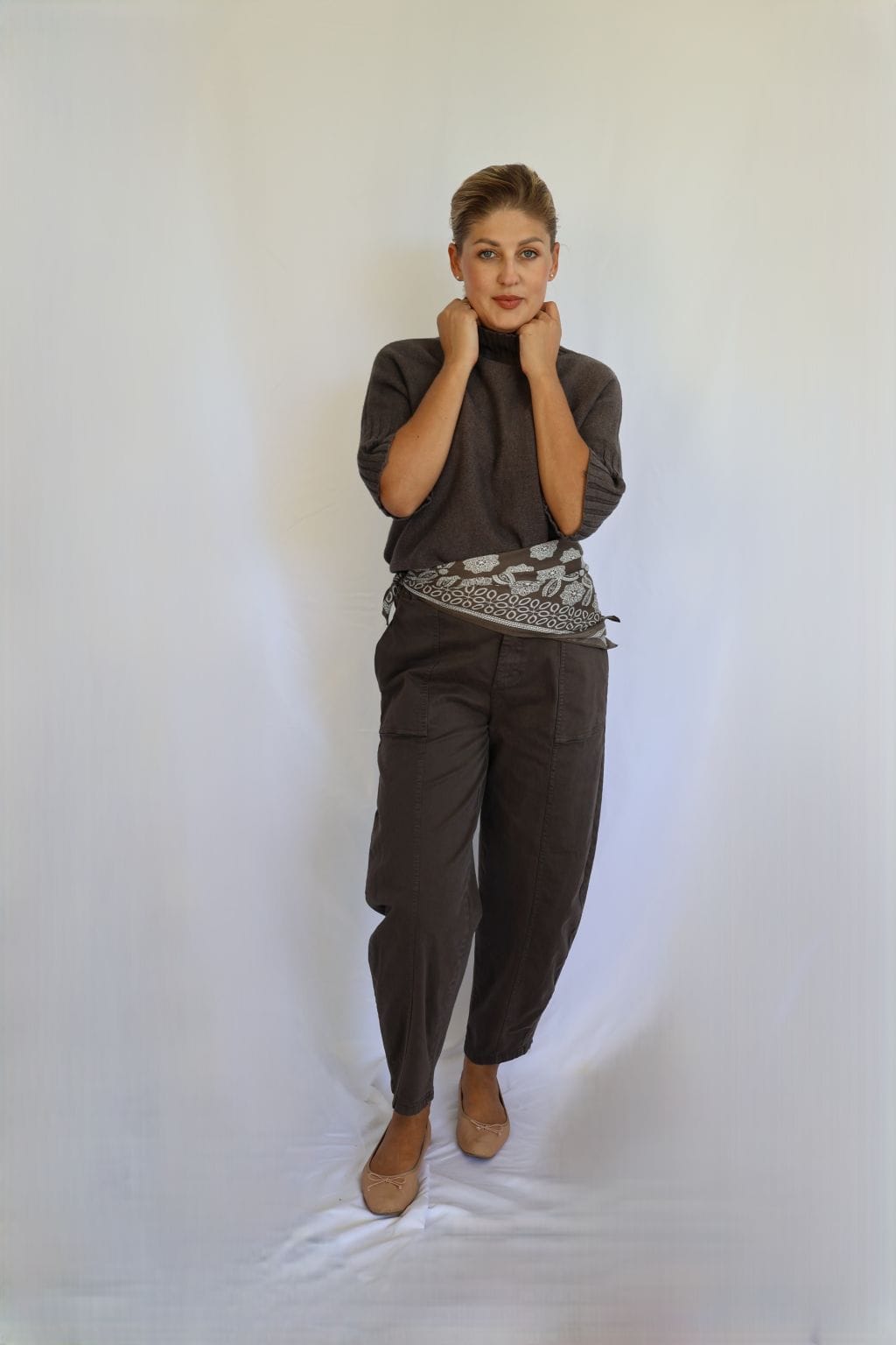 Jersey de punto marrón de mujer con manga corta hasta el codo y cuello chimenea de canalé, combinado con pantalón marrón y cinturón estampado.