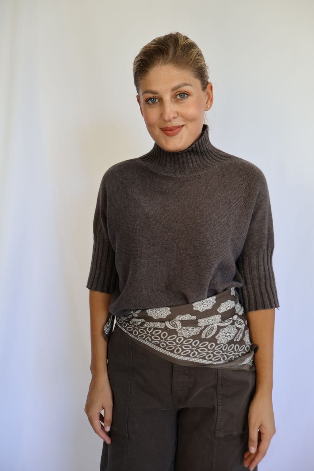 Jersey de punto marrón de mujer con manga corta hasta el codo y cuello chimenea de canalé, combinado con pantalón marrón y cinturón estampado.