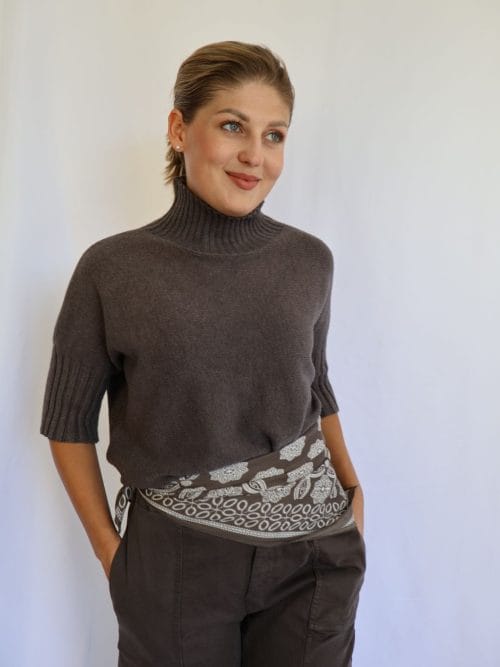 Jersey de punto marrón de mujer con manga corta hasta el codo y cuello chimenea de canalé, combinado con pantalón marrón y cinturón estampado.