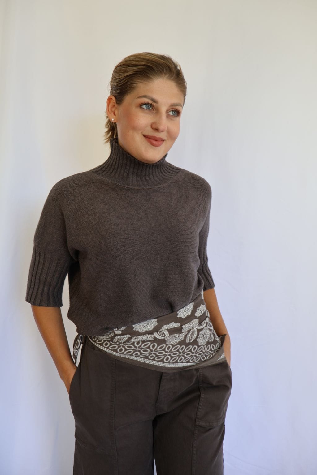 Jersey de punto marrón de mujer con manga corta hasta el codo y cuello chimenea de canalé, combinado con pantalón marrón y cinturón estampado.