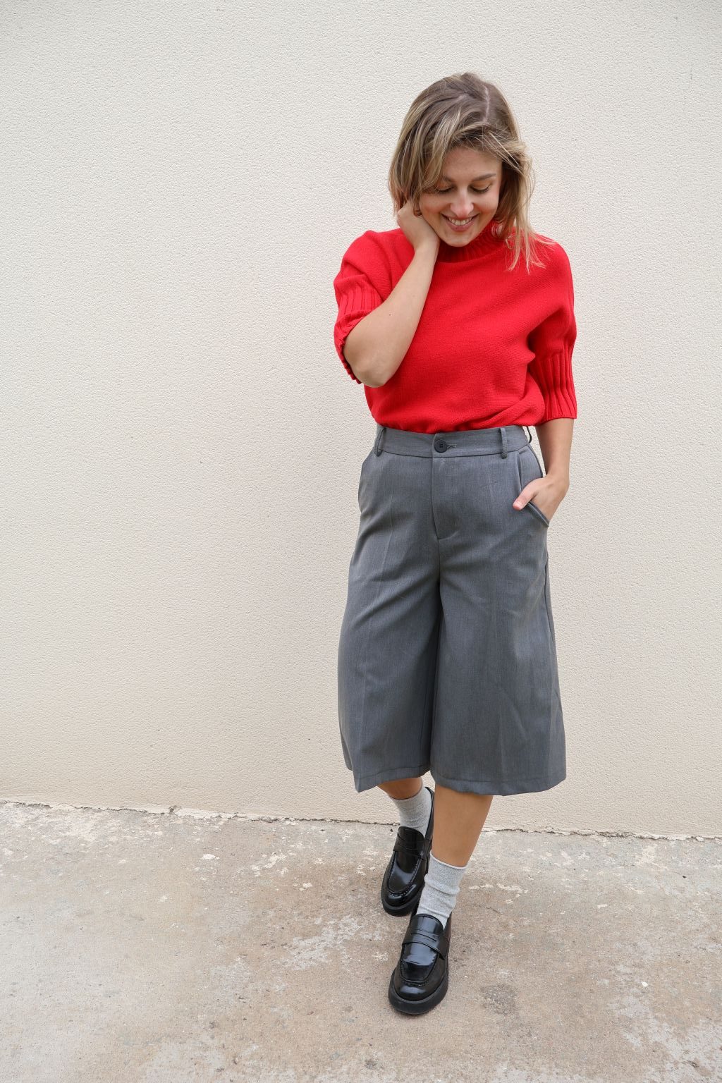 Bermuda gris de mujer PANTTAC de corte ancho, con bolsillos y largo por debajo de la rodilla, combinada con jersey rojo y mocasines negros.